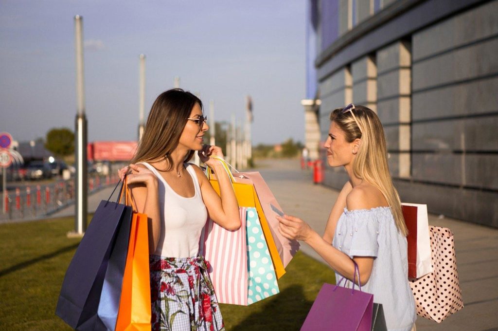 Two women talking on the phone while holding shopping bags.