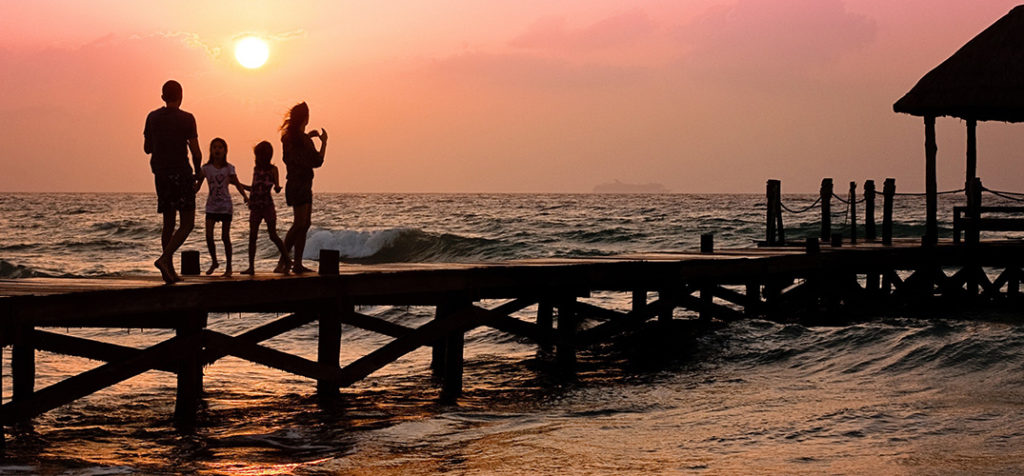 A family is standing on a pier at sunset.