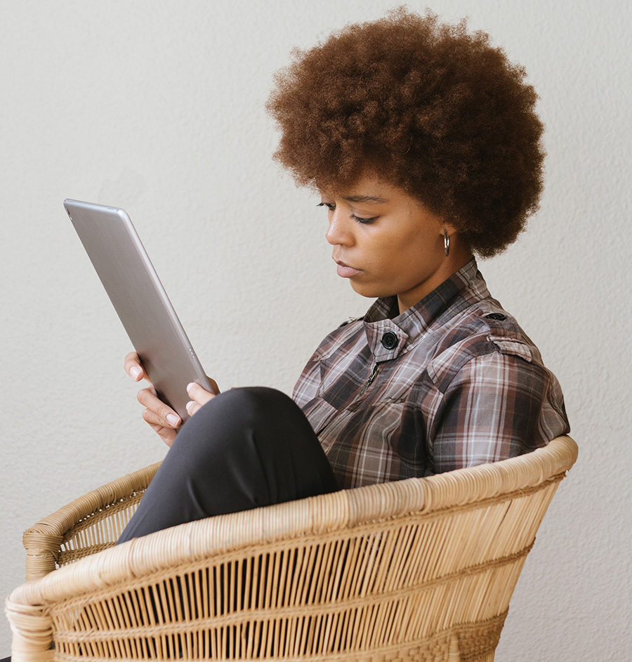 A woman sitting in a wicker chair using a tablet computer.