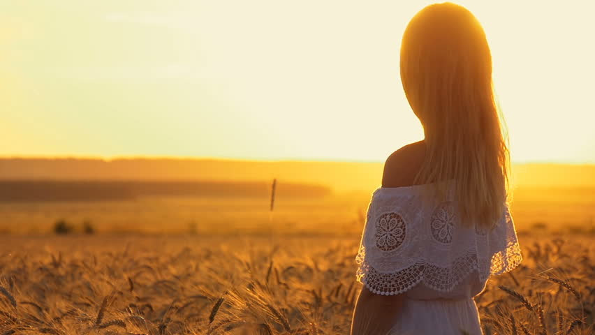 A woman is standing in a wheat field at sunset.